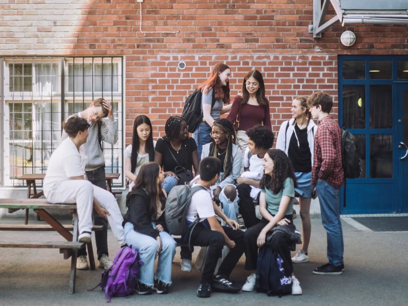 Eine Gruppe von Jungen und Mädchen unterschiedlicher Herkunft sitzt während der Pause auf dem Campus der Junior High School.