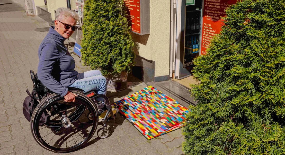 Rita Ebel im Rollstuhl vor bunter Rollstuhlrampe aus Lego