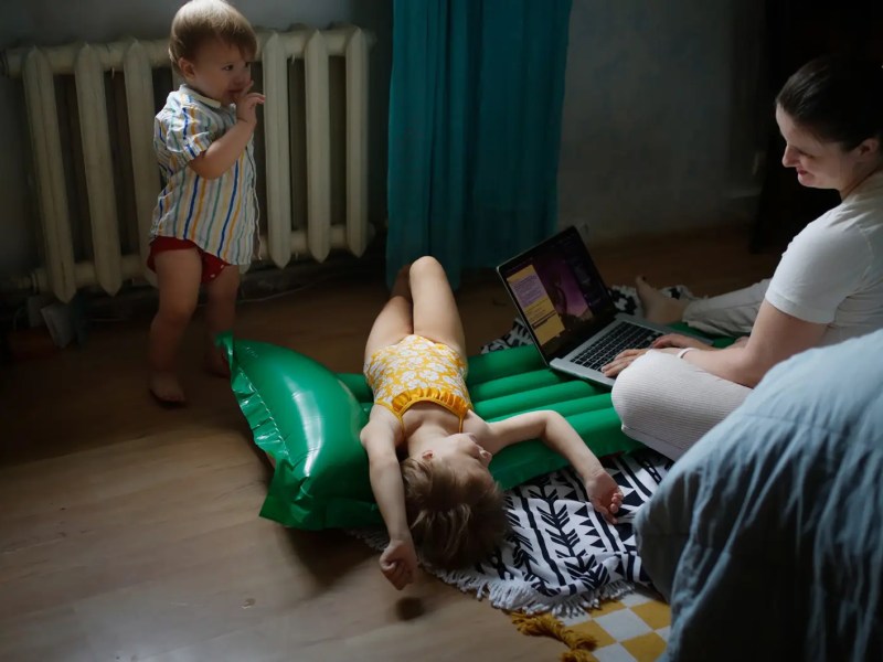 Mutter arbeitet am Laptop, während ihre Kinder um sie herum spielen.