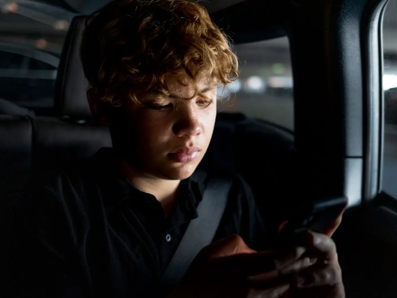 Teenager im Auto schaut auf sein Smartphone.