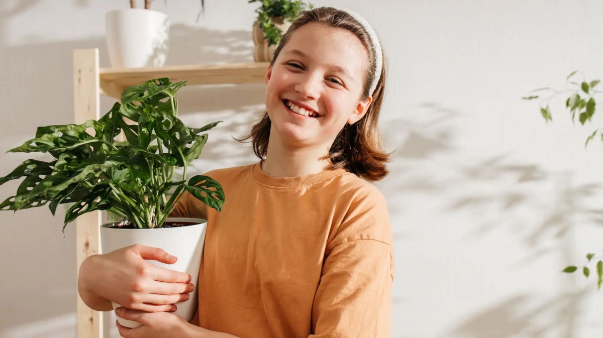 Teenagermädchen trägt freudestrahlend einen Blumentopf.
