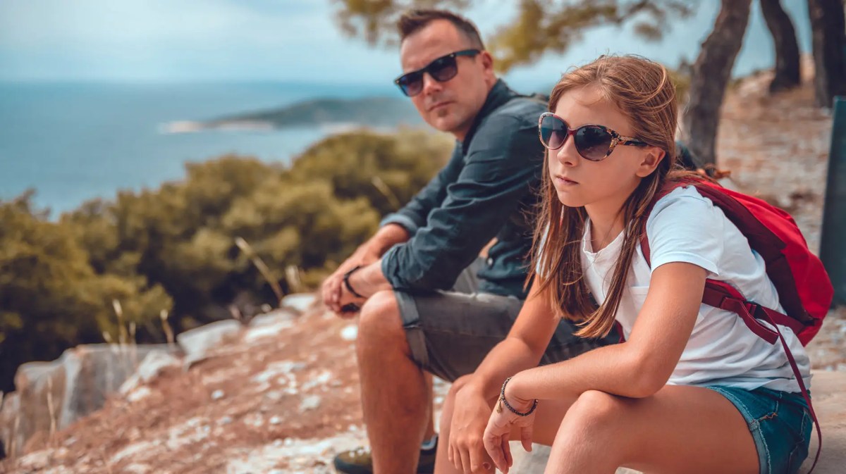 Vater und Tochter auf einem Berg. Die Tochter im teenageralter sieht genervt aus.
