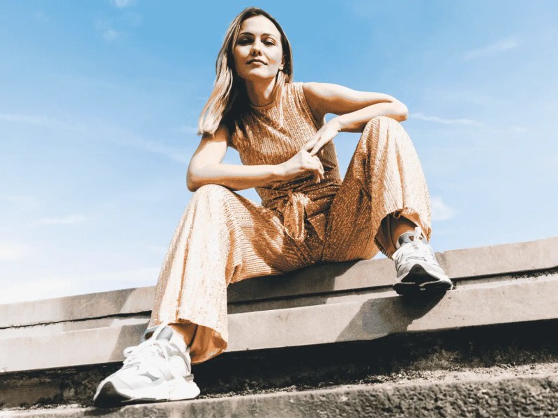 Frau in sommerlichen Jumpsuit sitzt auf Stra&szlig;e.