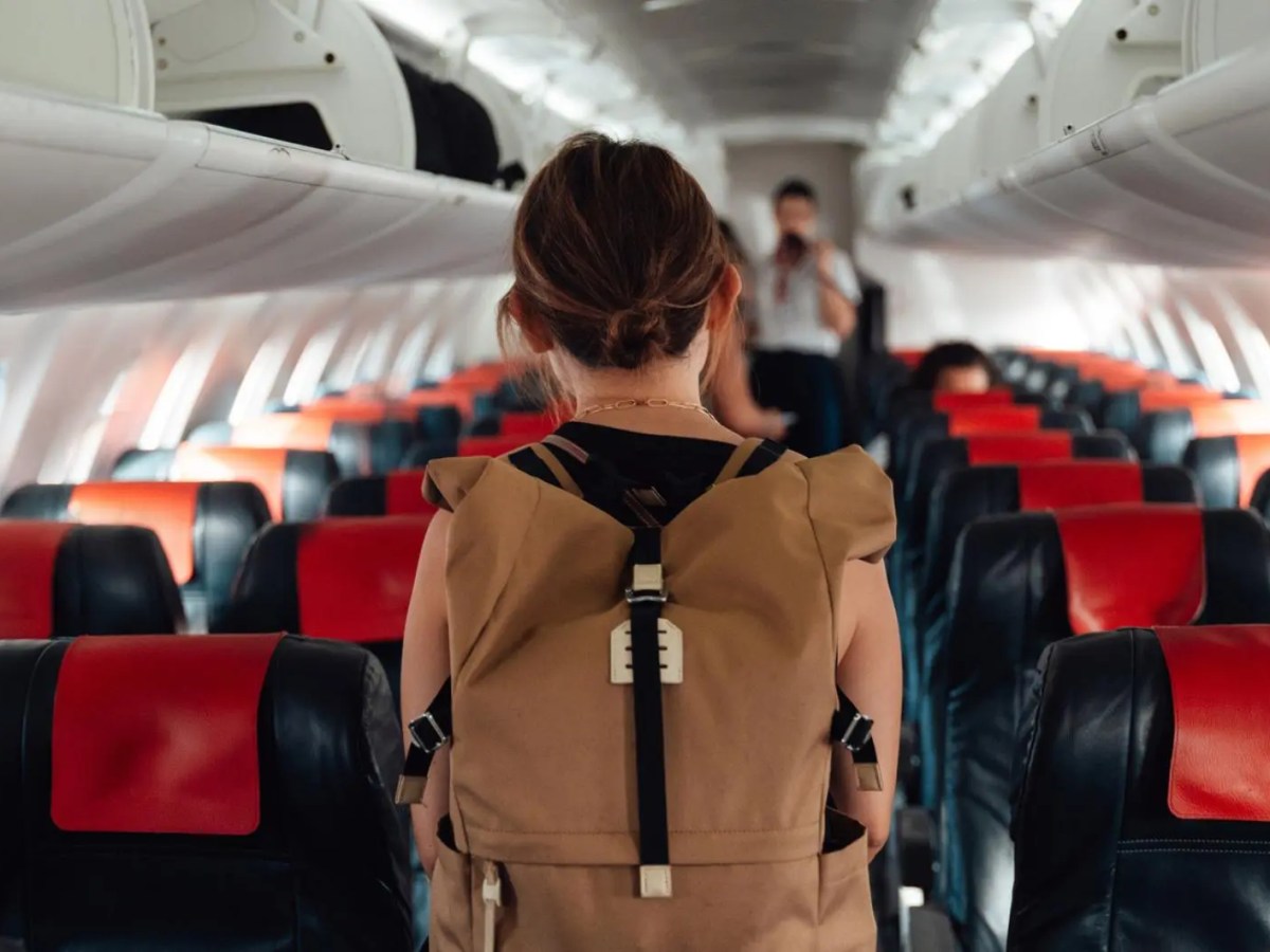 Frau mit Rucksack von hinten l&auml;uft durch ein Flugzeug.