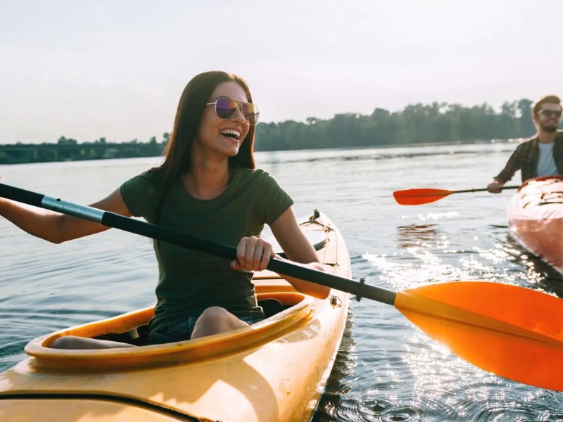 Vorne rechts ist eine Frau in einem Kajak auf dem See, dahinter ein Mann. Beide haben Spa&szlig;.