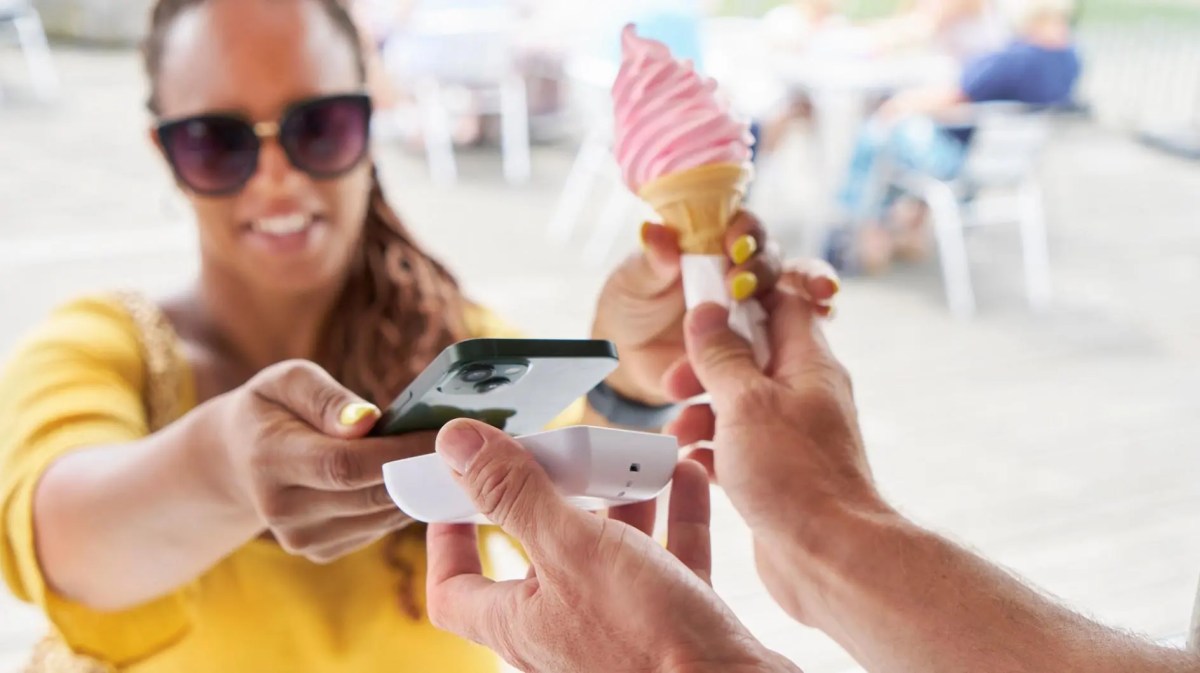 Frau bezahlt ein Eis an einem Stand draußen.