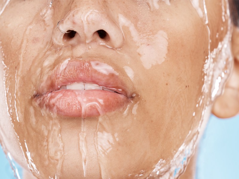 Frau mit Wasser, das &uuml;ber dem Gesicht l&auml;uft und die Haut gl&auml;nzen l&auml;sst