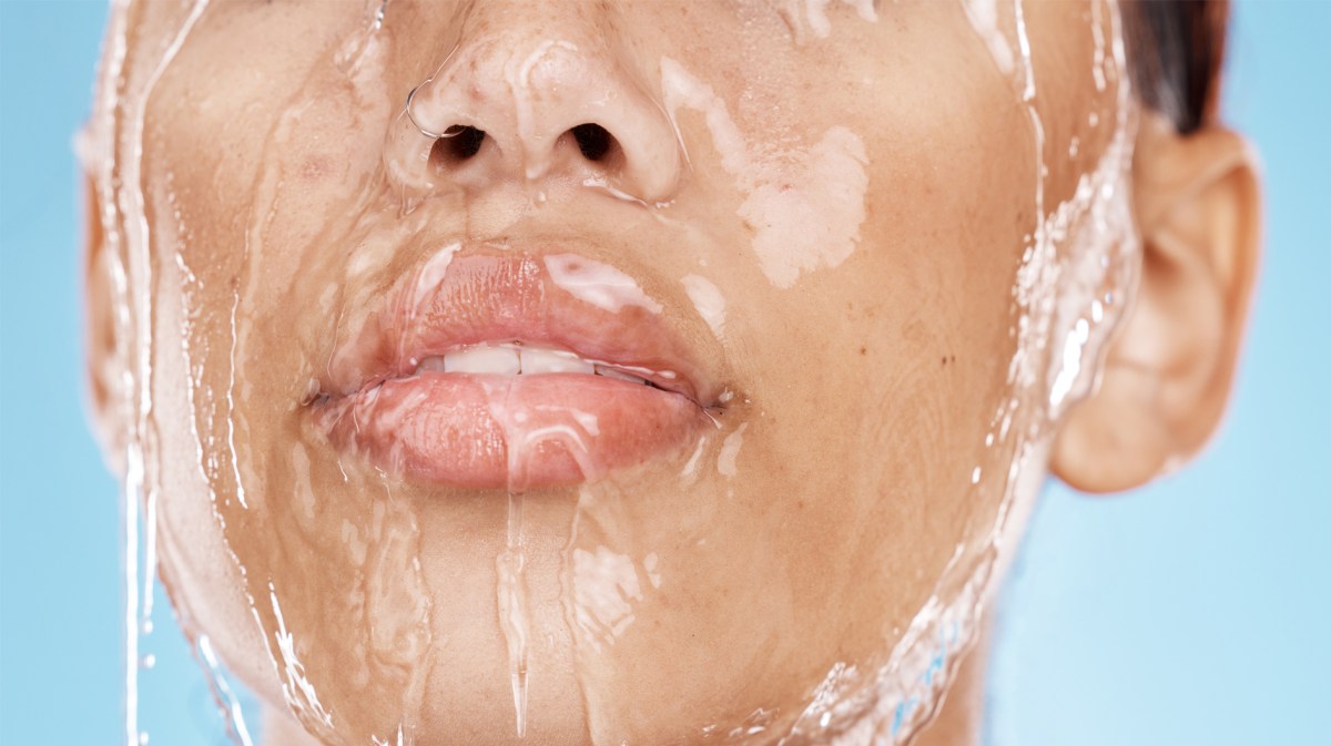Frau mit Wasser, das über dem Gesicht läuft und die Haut glänzen lässt