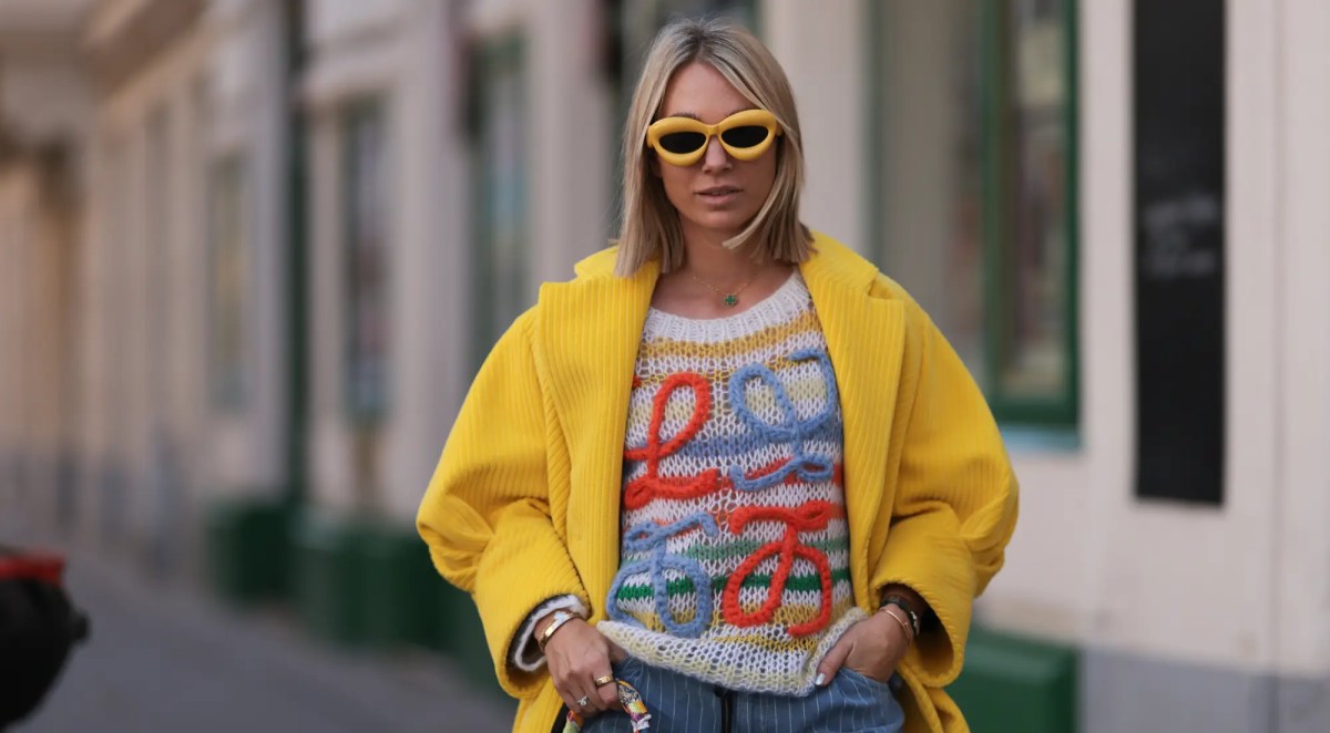 Frau mit buntem Pulli, gelber Jacke, gelber Sonnenbrille und Jeans