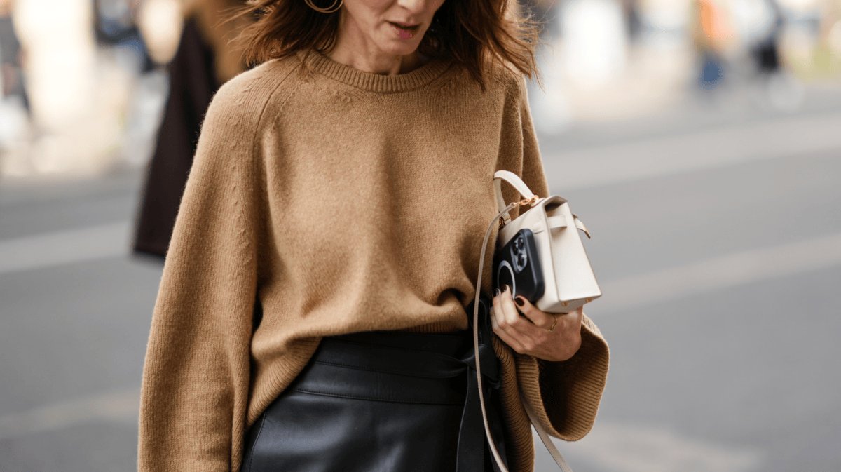 Modische Frau trägt Tasche und Handy in der Hand